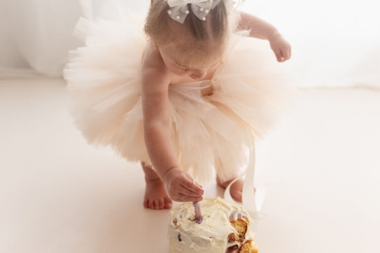 Photograph showing what a cake smash photoshoot looks like, with a young girl in a tutu playing with her cake and candle.