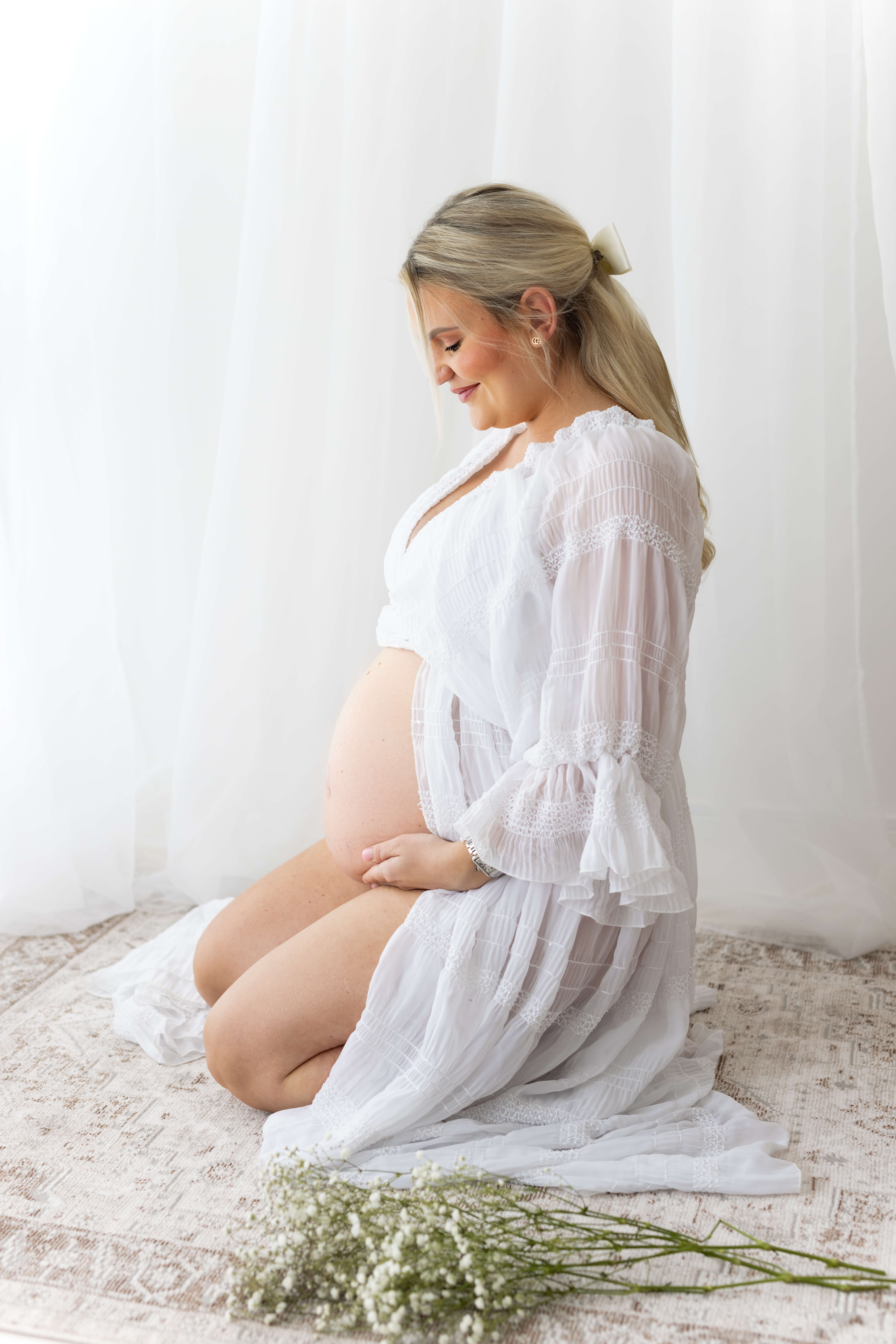 White dress for maternity photoshoot used, with mum kneeling and looking at her bump