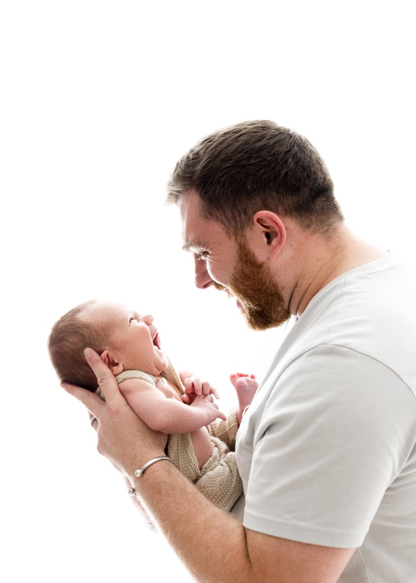 Newborn baby and dad looking at each other smiling and laughing