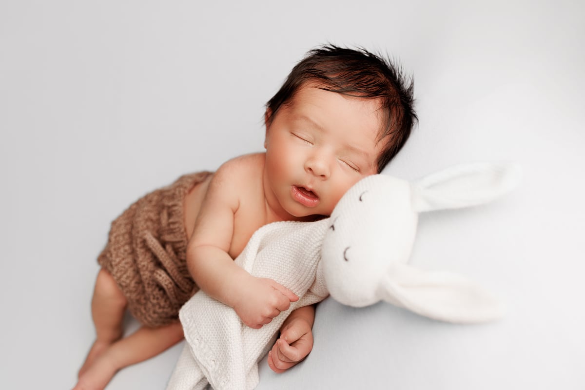 Newborn photography with props, dressed in a brown pair of shorts, holding a white toy rabbit