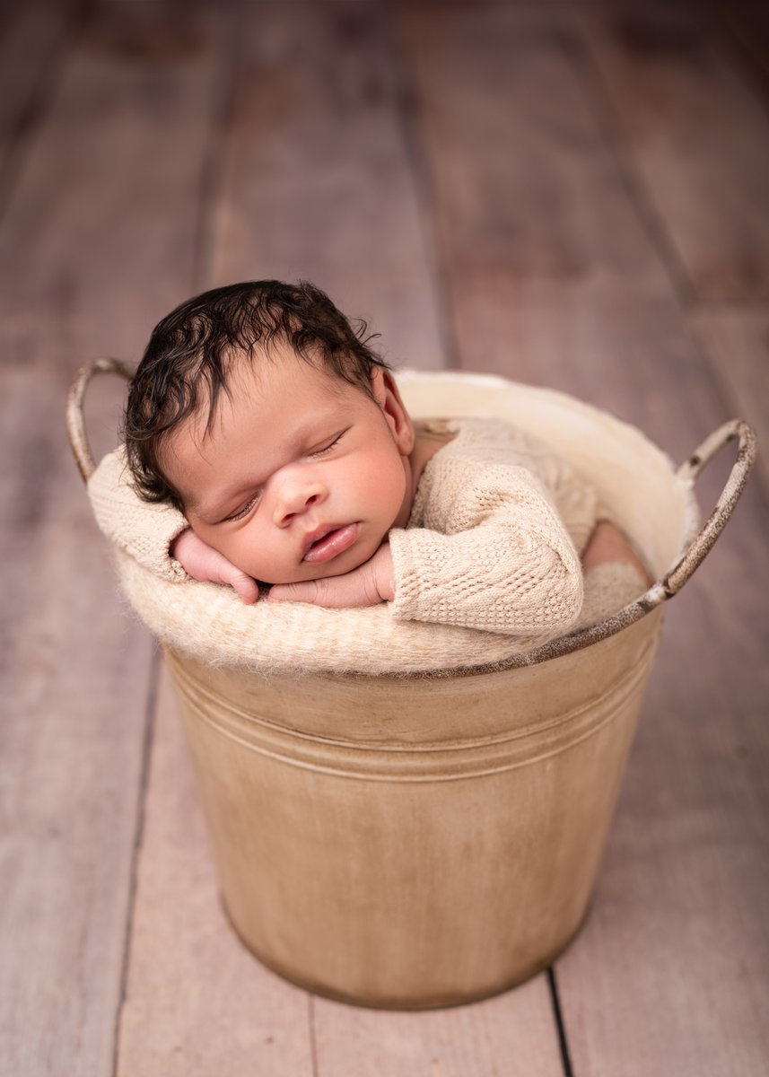 Newborn baby posed in a soft and cosy basket for photoshoot