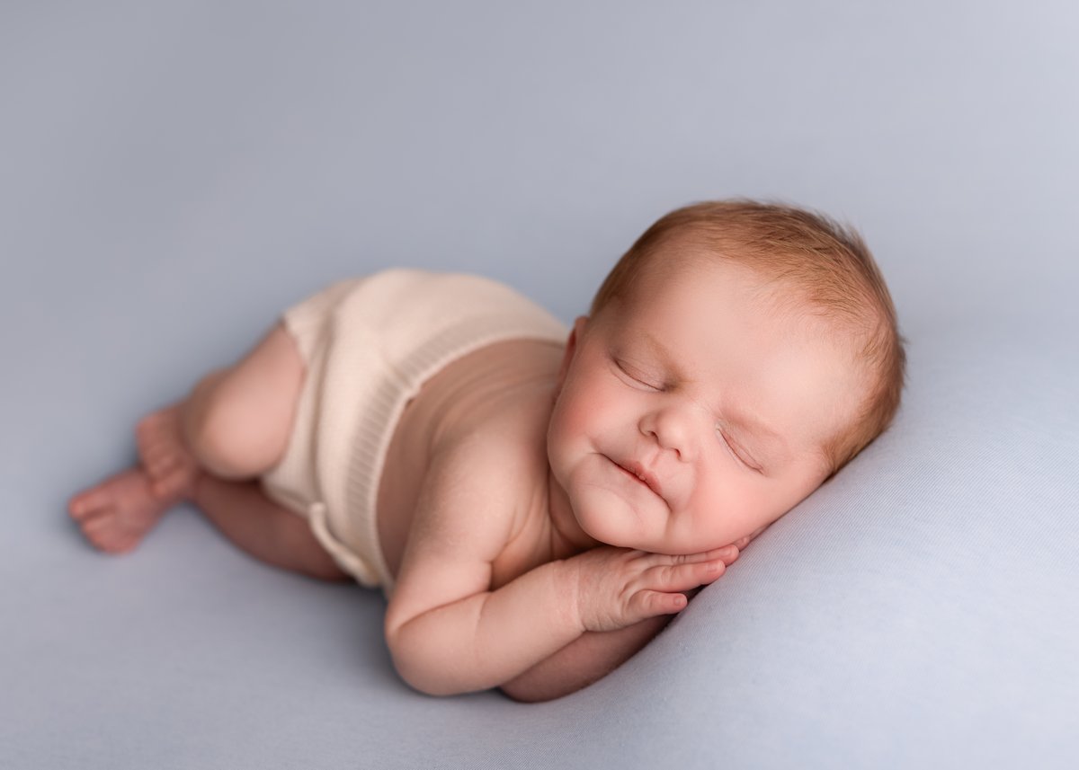 Baby boy photoshoot with a blue soft cushion, posed in a sleeping position