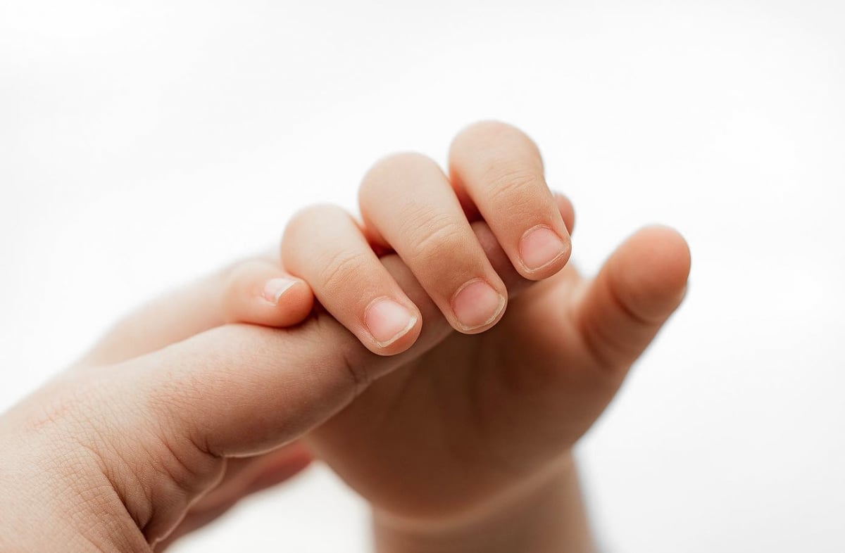 Close-up photograph of a newborn baby's hand and finger nails, held by their parent