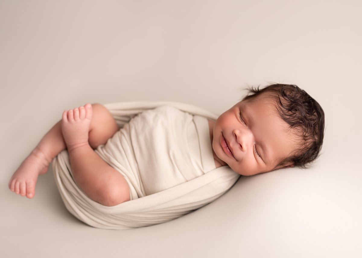 Photograph of a newborn baby, smiling in a linen wrap