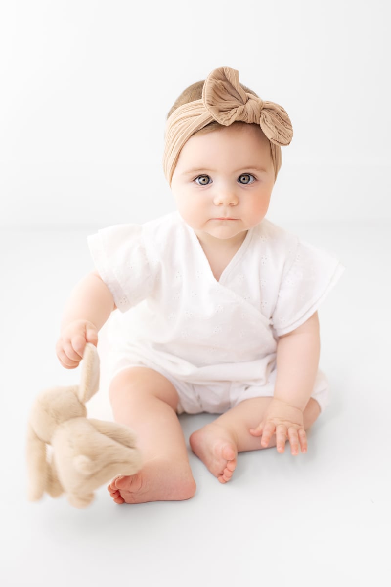 Baby photographed with a cuddly rabbit toy, wearing a bow on their head