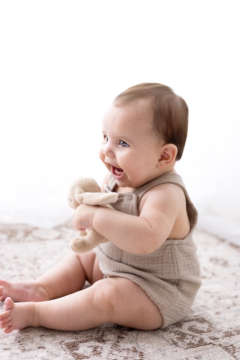 Baby sitting and smiling happy at photoshoot with cuddly rabbit toy