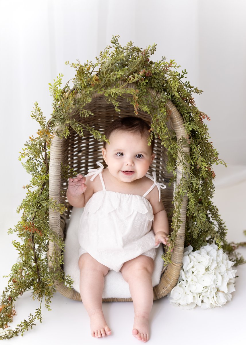 Shows a baby sitting inside of an outdoors-themed prop for sitter photoshoot