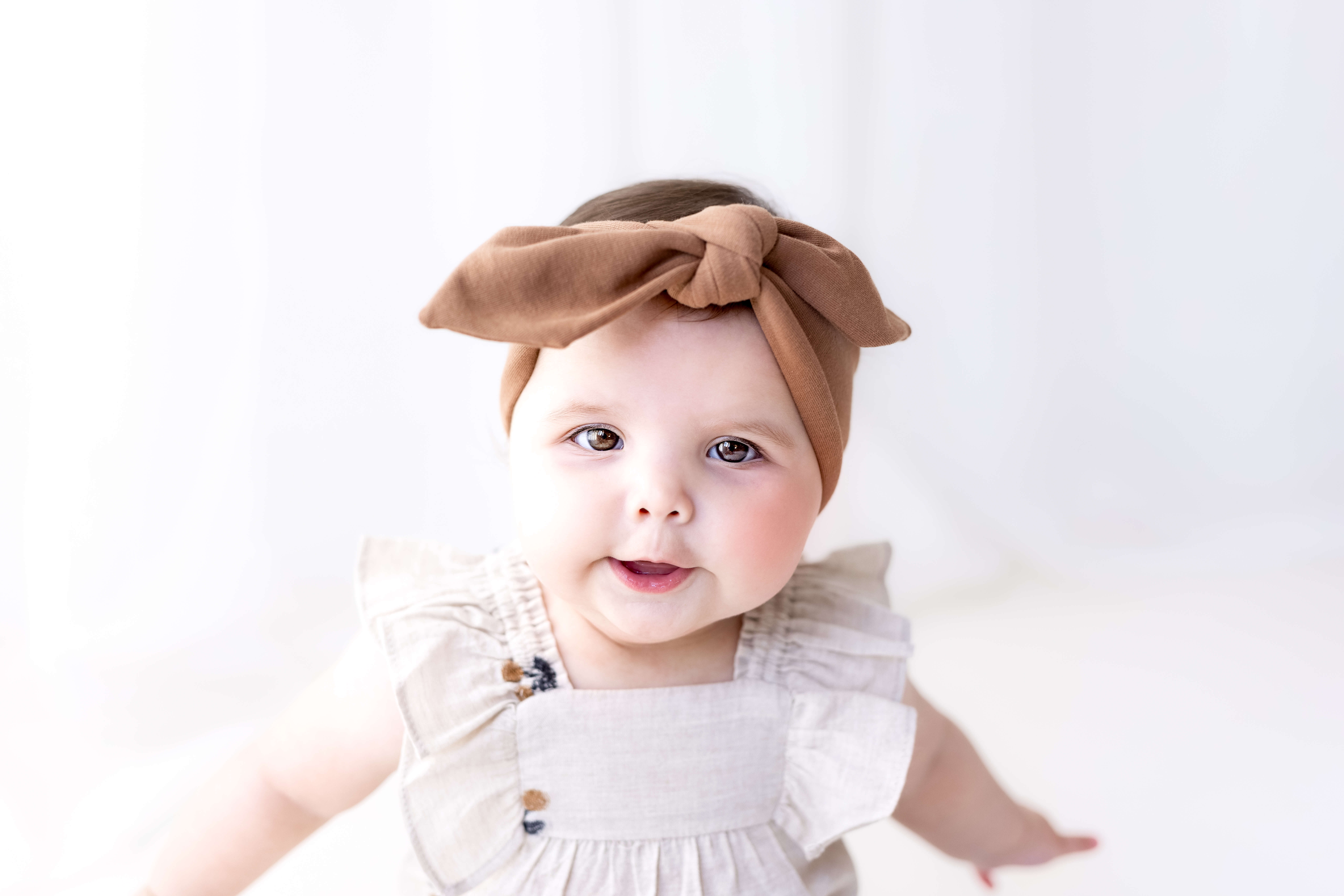 Baby at a sitter photoshoot in an outfit with a bow, in neutral soft ground earthy colours