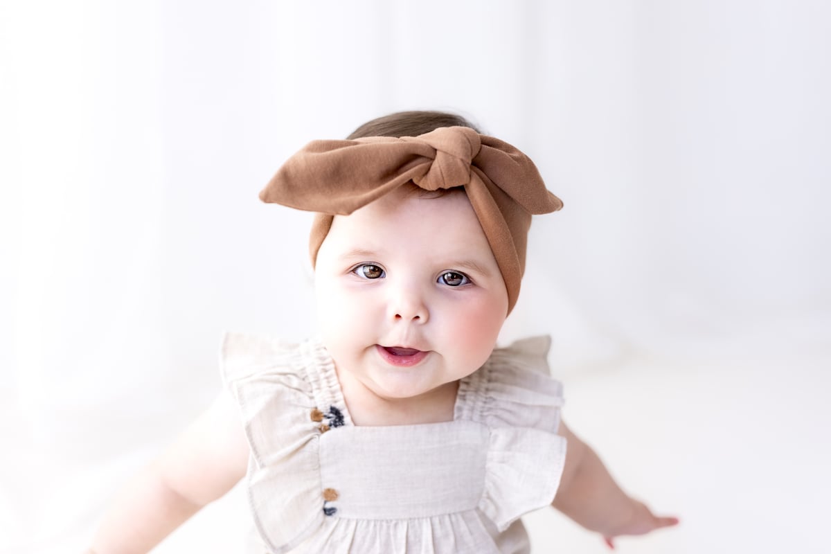 Baby at a sitter photoshoot in an outfit with a bow, in neutral soft ground earthy colours